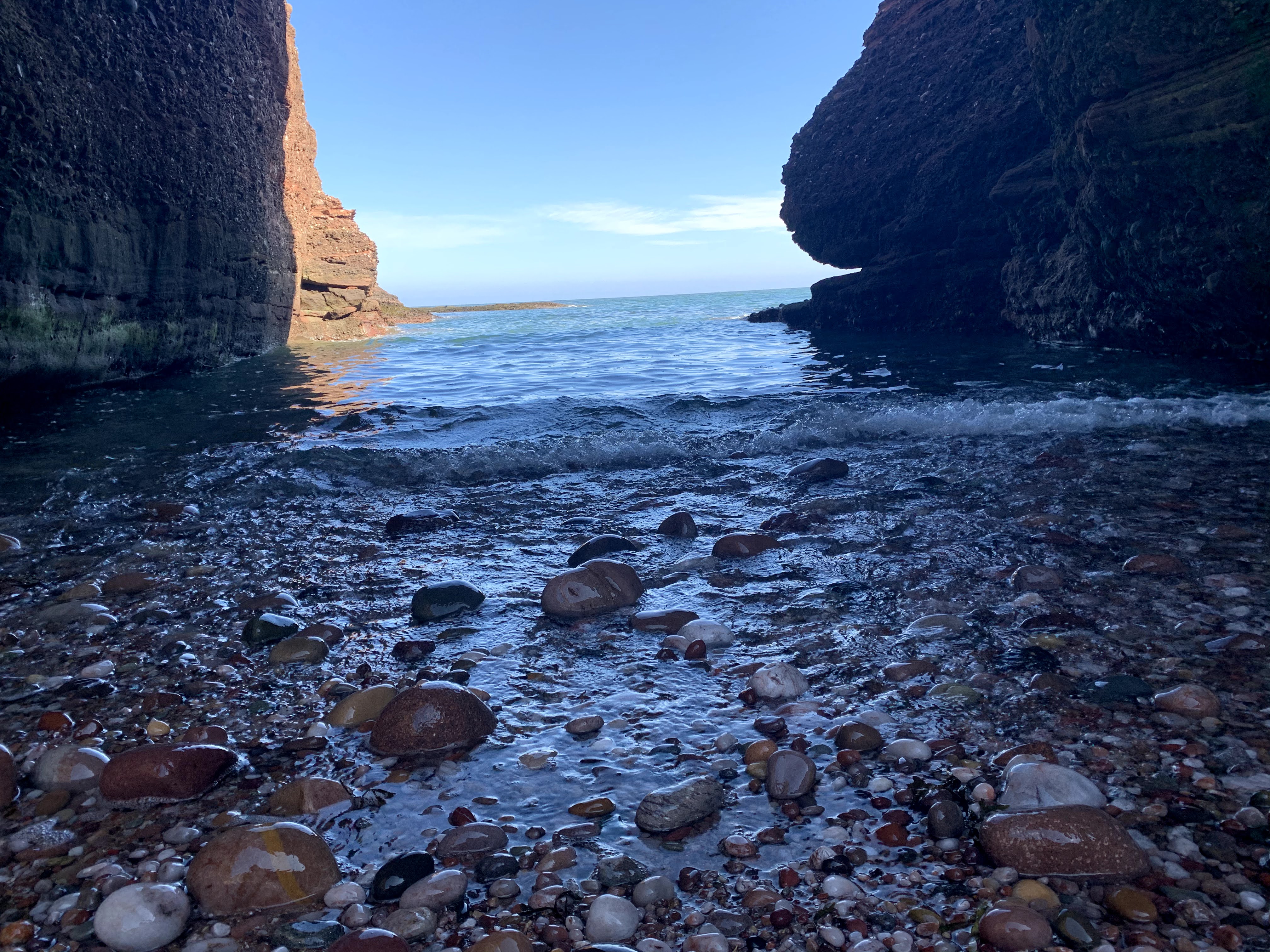 Photo of a rocky shore Photograph of a sea arch. On either side of the image is large rocks. In the middle is a small rocky beachfront extending out into water.