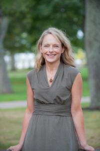 Blonde Lori Mayne wears a grey dress and smiles at the camera.