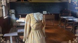 Photo of the display in the schoolhouse in Lower Bedeque, PEI stylized A human-sized mannequin without a head in Victorian clothing standing in front of a school desk in an old classroom.