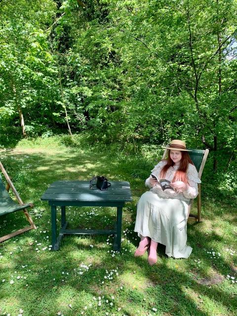 Wallis Chelsea Visual Chelsea Wallis wearing a straw hat and reading a book while sitting in a sunny garden.