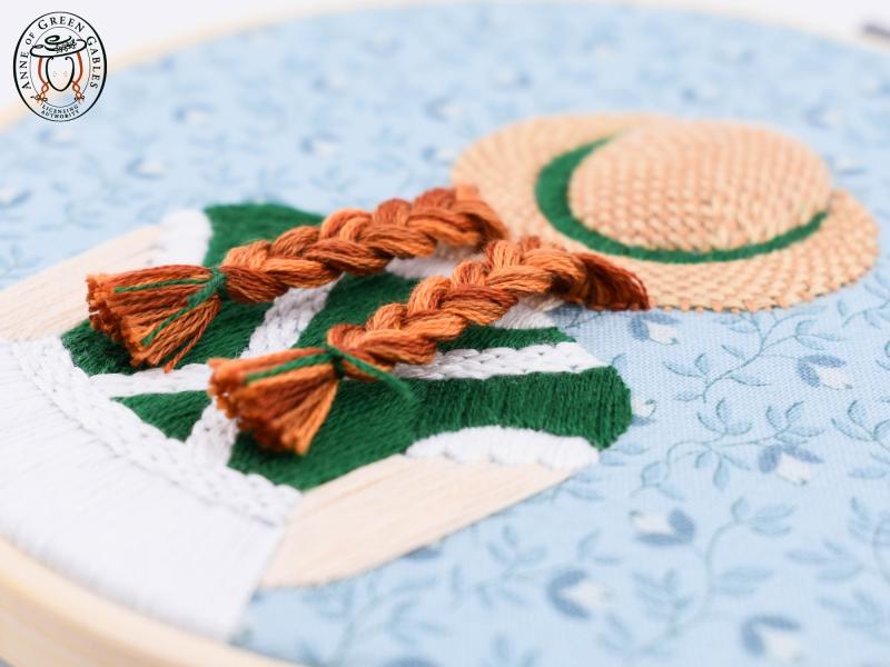 Rebecca MacDonald Embroidery depicting red braids under a straw hat.