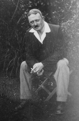 Cavert Image 10 Photograph of George MacMillan sitting on a bench outdoors holding a cigarette.