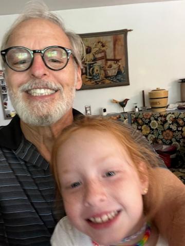 Steve Valliere The poet is a smiling man with grey hair and beard and black-framed glasses. His granddaughter is a smiling girl with red hair and freckles.