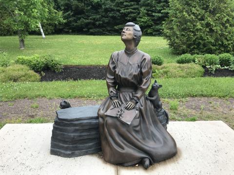 Sellers Reflections Image 4 Photo of a bronze statue of L.M. Montgomery sitting on a bench, face upturned, with a book in her lap, and two cats nearby.